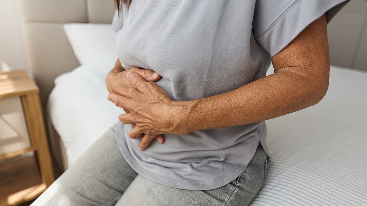 Senior woman holding her stomach and sitting on a couch at home
