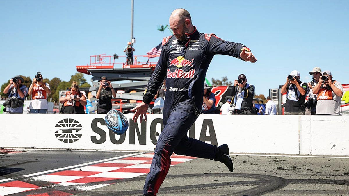 Shane Van Gisbergen kicking a rugby ball at Sonoma Raceway.