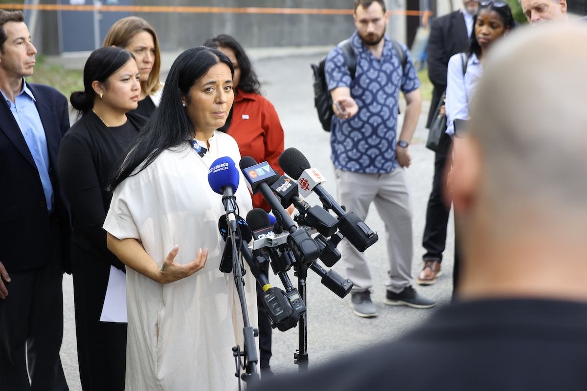 Soraya Martinez Ferrada speaks at an outdoor press conference, surrounded by city hall officials, journalists and microphones.