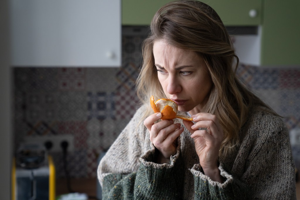 A woman with COVID-19 symptoms tries to smell a tangerine.