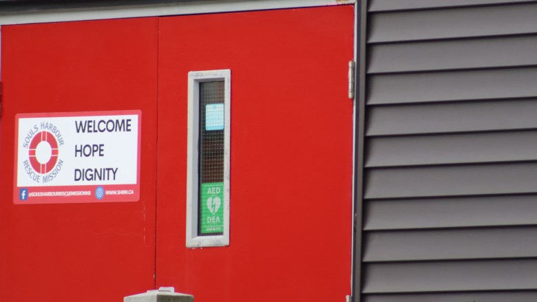 A main door to a building is painted in bright red and has a white sign on it that says "Welcome, hope, dignity."