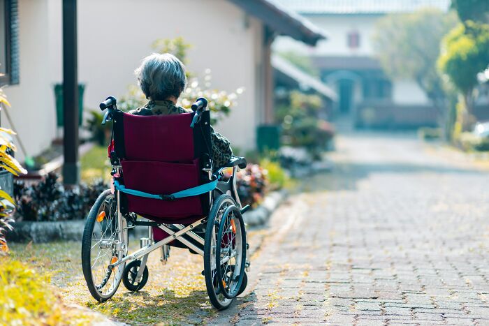 Elderly person in a wheelchair outside a home, illustrating dementia care and mobility