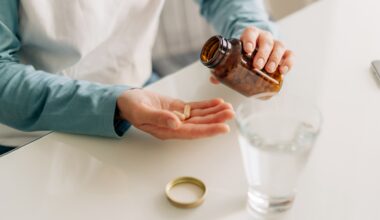 A person pours capsules from a brown bottle into their palm, with a glass of water nearby.