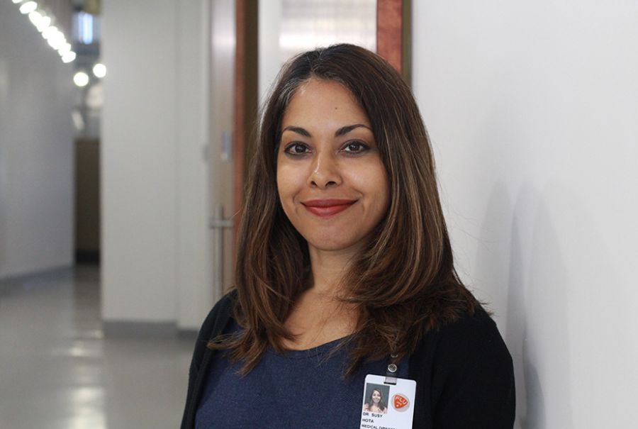 Dr. Susy Hota smiling in a hallway at UHN with her name badge on her sweater.