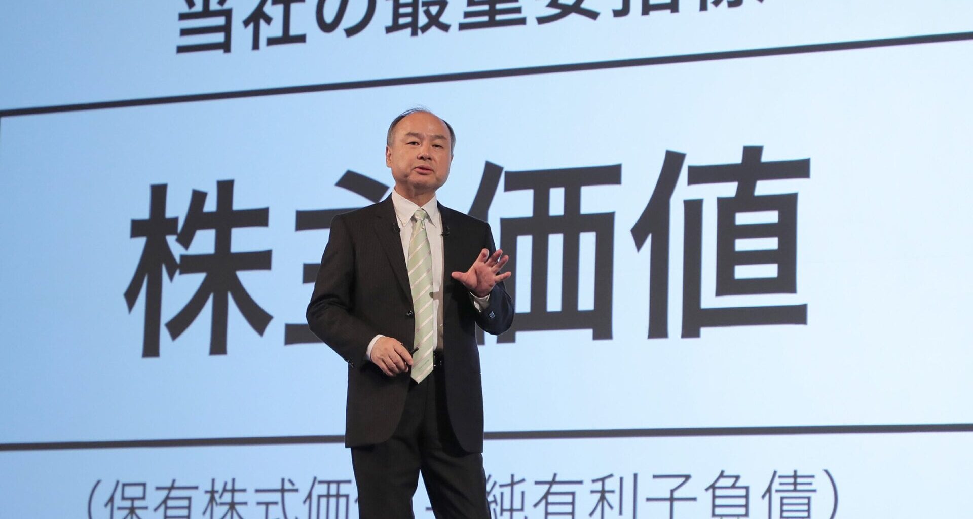 Masayoshi Son speaking in front of a screen with japanese writing