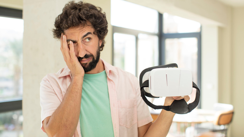 A man looks doubtful while holding a VR headset.