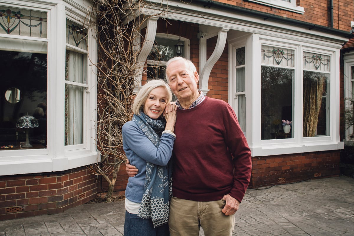 A couple poses on a sidewalk outside a shop.