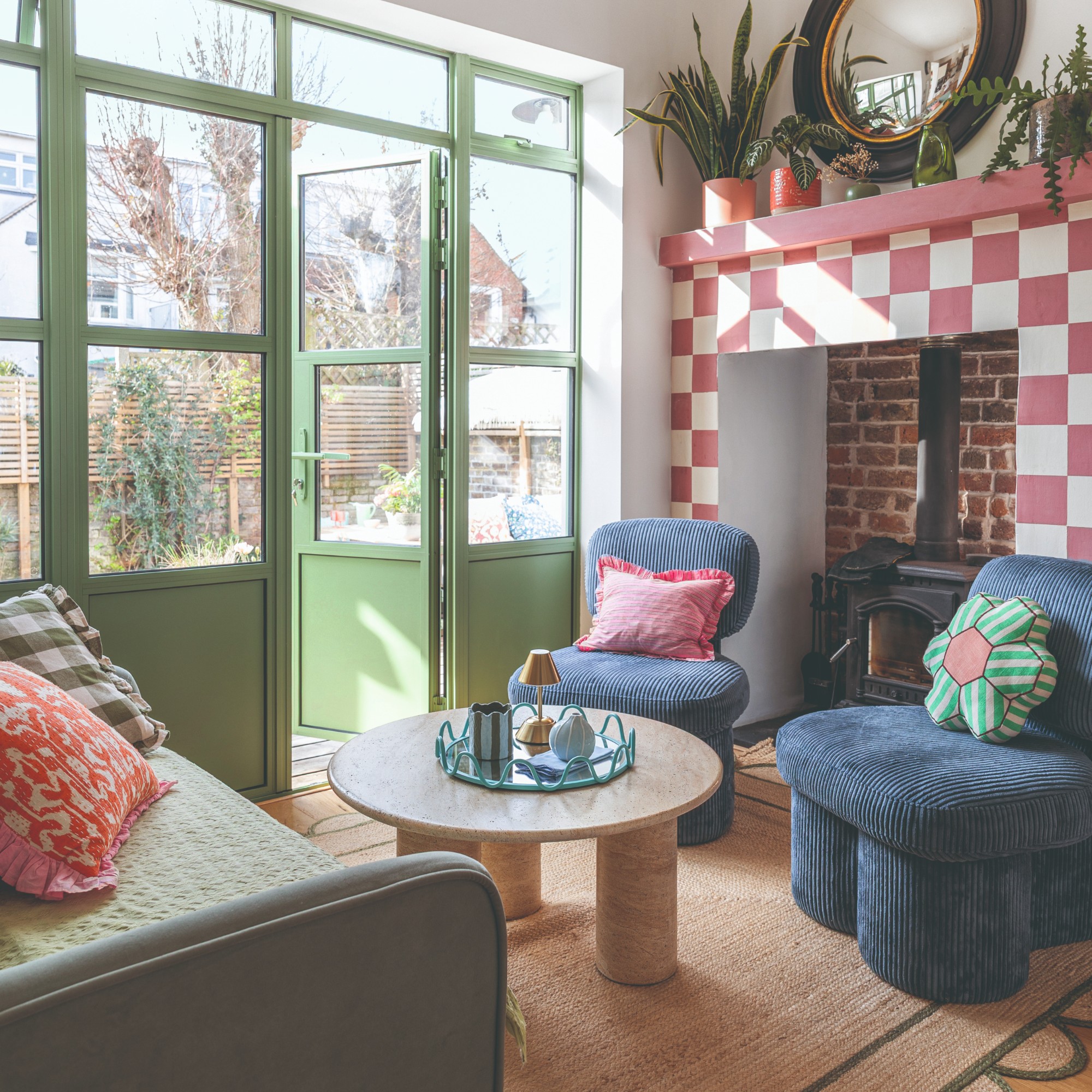A living room with a fireplace ainted in a pink chequerboard print with two blue corduroy chairs and a green sofa