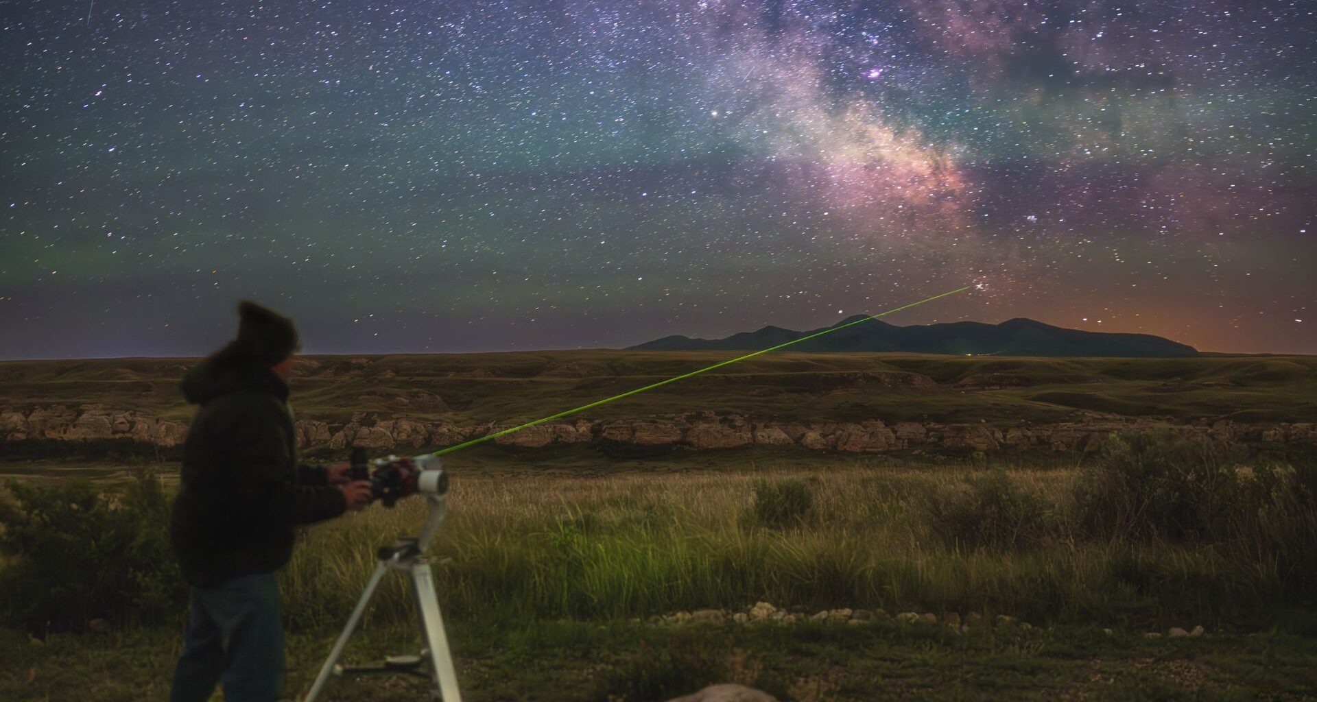 a man stands shining a laser to messier 7 which is in the tail of the scorpius constellation.