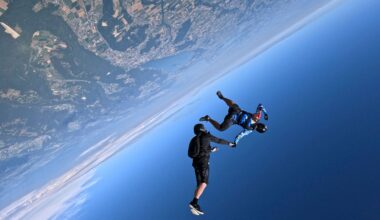 Two people hold hands while skydiving over Earth, a view of its surface next to the blue sky is seen.
