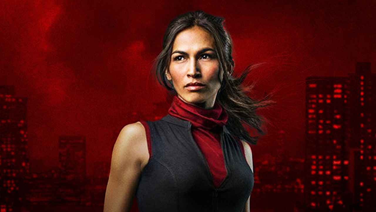 Elektra standing in front of a red background.