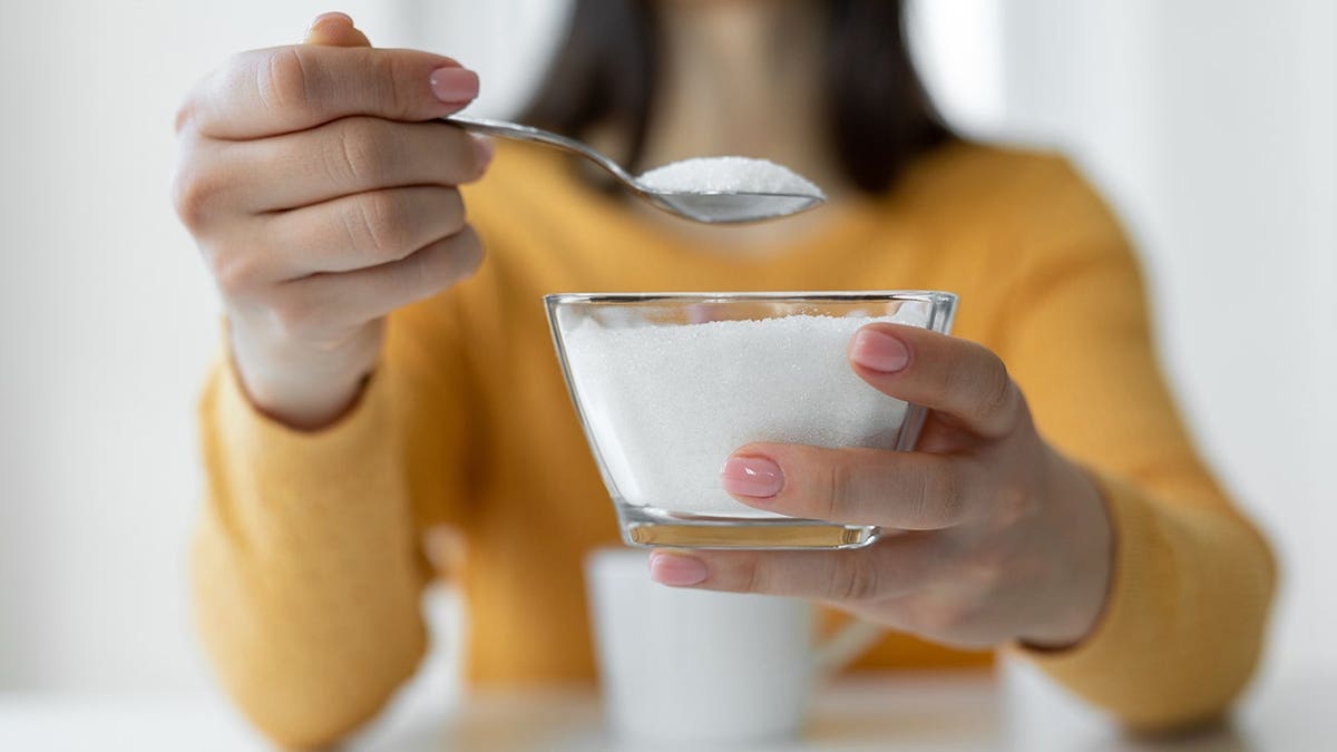 Woman adding refined sugar to a cup of coffee.