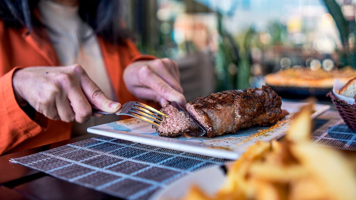 A woman used a knife and fork to cut a steak.