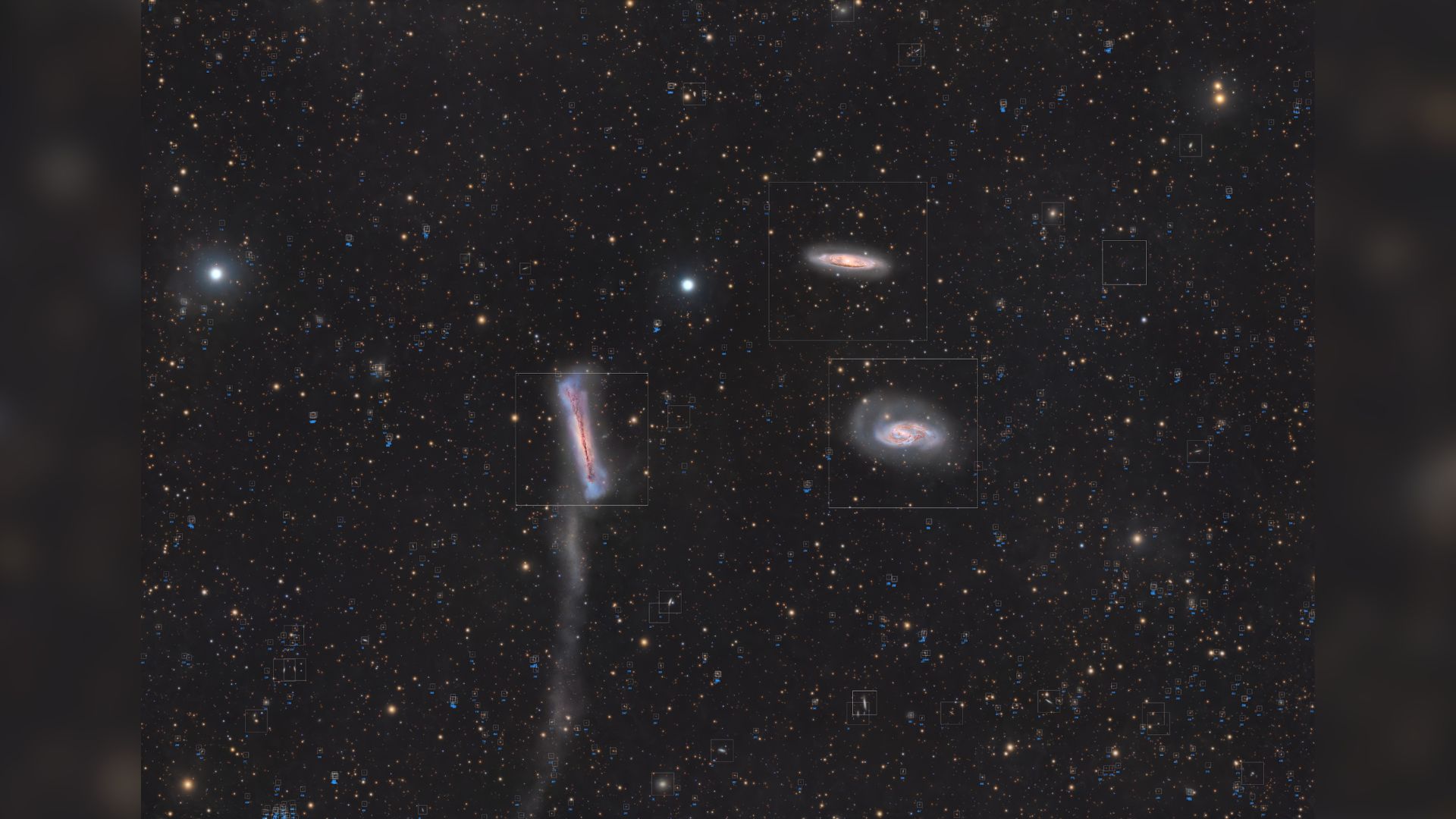 A trio of galaxies are pictured shining in deep space against a starfield dotted with more distant galaxies.