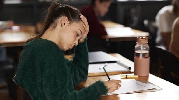 Tensed teenage girl writing on paper while sitting at desk during exam in classroom