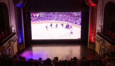 People sitting in movie theatre watching hockey game on big screen.