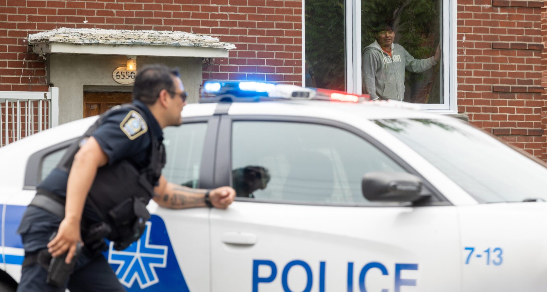 A resident watches from a window as Montreal police officer deploys at a shooting in Côte-des-Neiges.