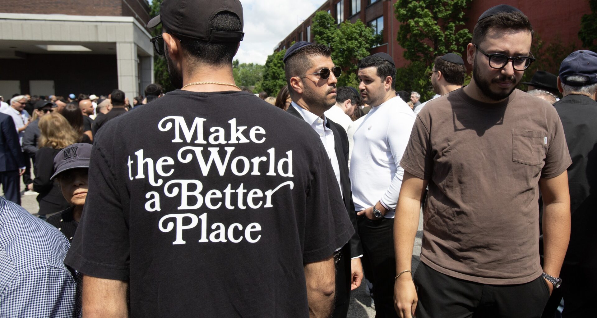 "Make the World a Better Place" is inscribed on the back of a T-shirt worn by a mourner outside the Paperman funeral home where family and friends gathered for the funeral of Michel Mizrahi