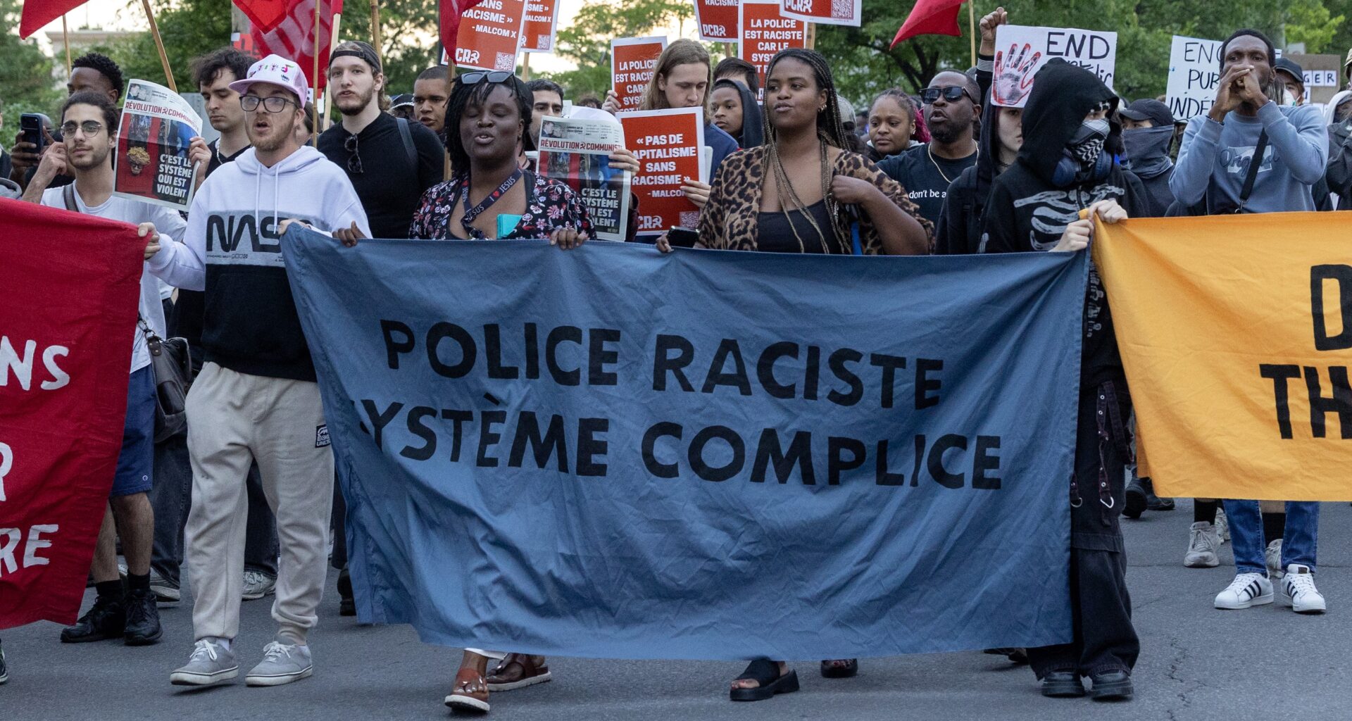 Anti-police racism marchers hold banners in Montreal North