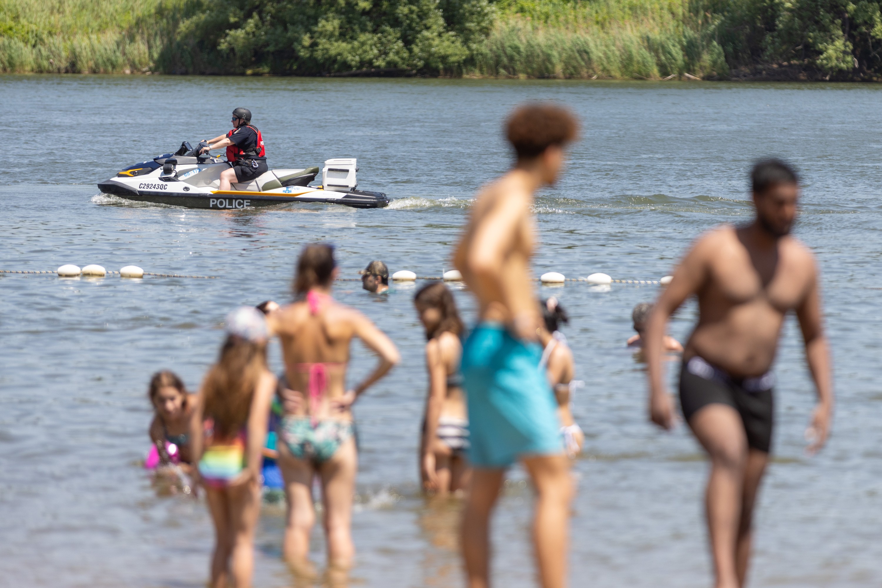 Swimmers in the foreground are slightly out of focus as a police officer on a jetski patrols a beach.