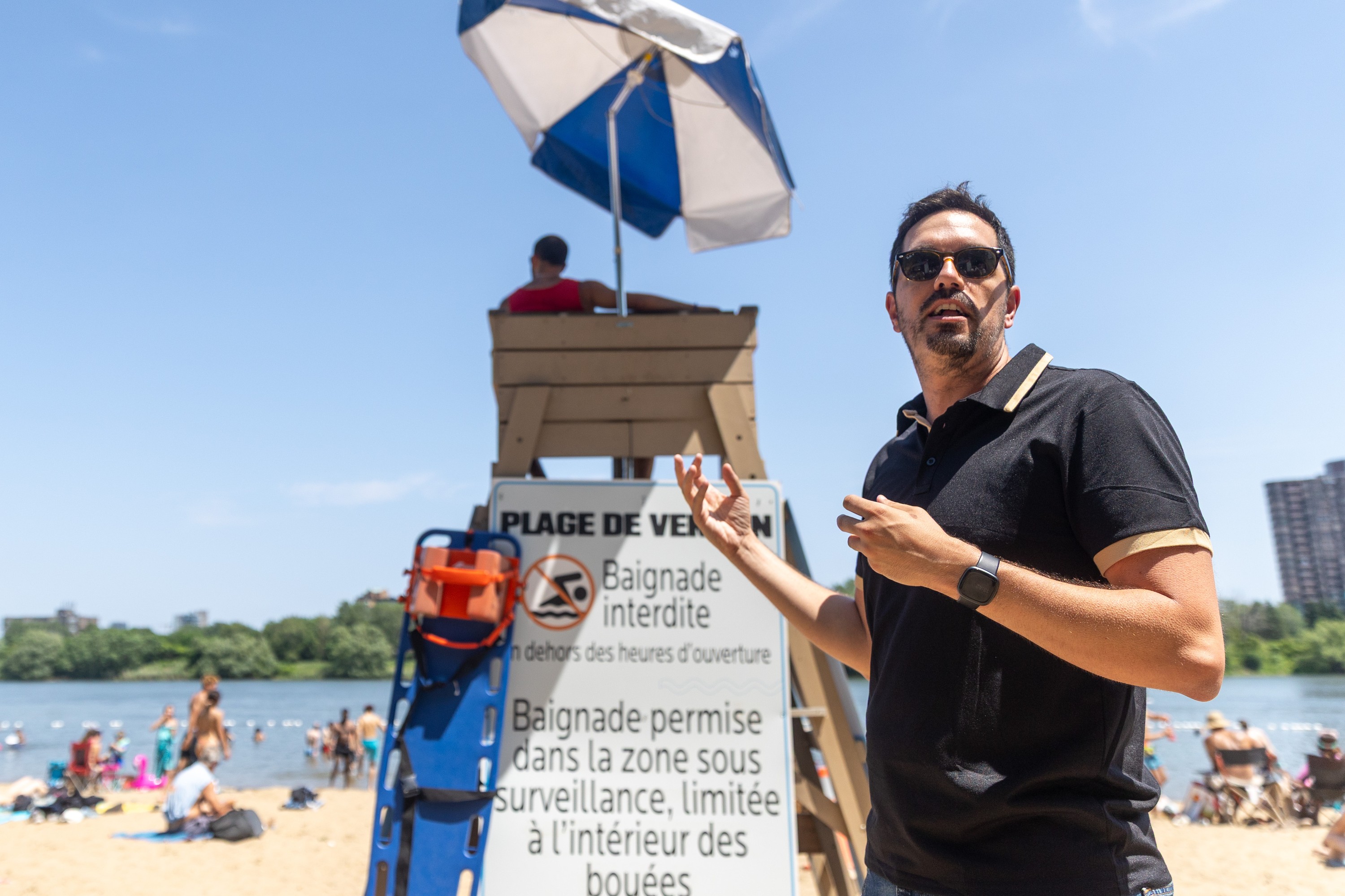 A man gestures while speaking. Behind him is a lifeguard station and safety devices.