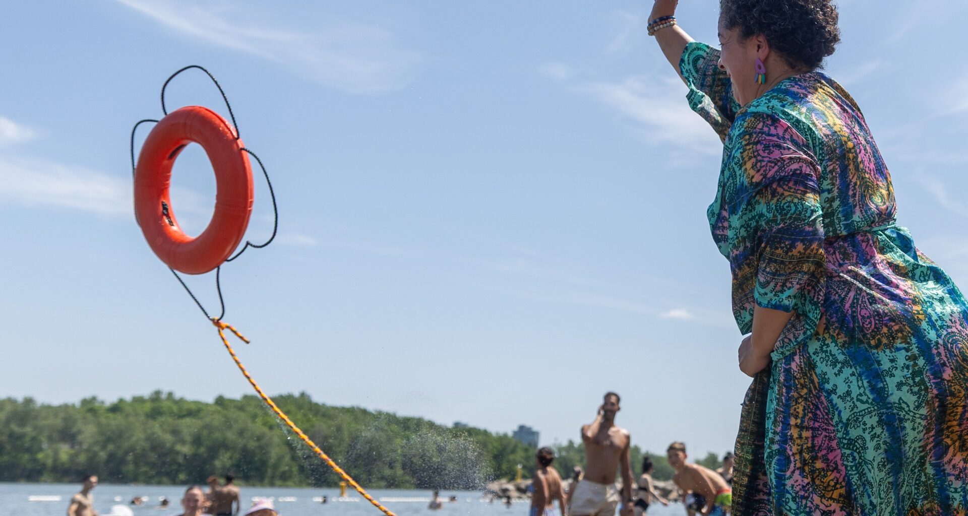 A woman throws a life preserver toward smiling swimmers at a beach.