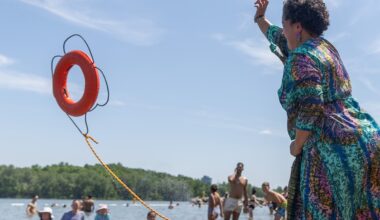 A woman throws a life preserver toward smiling swimmers at a beach.