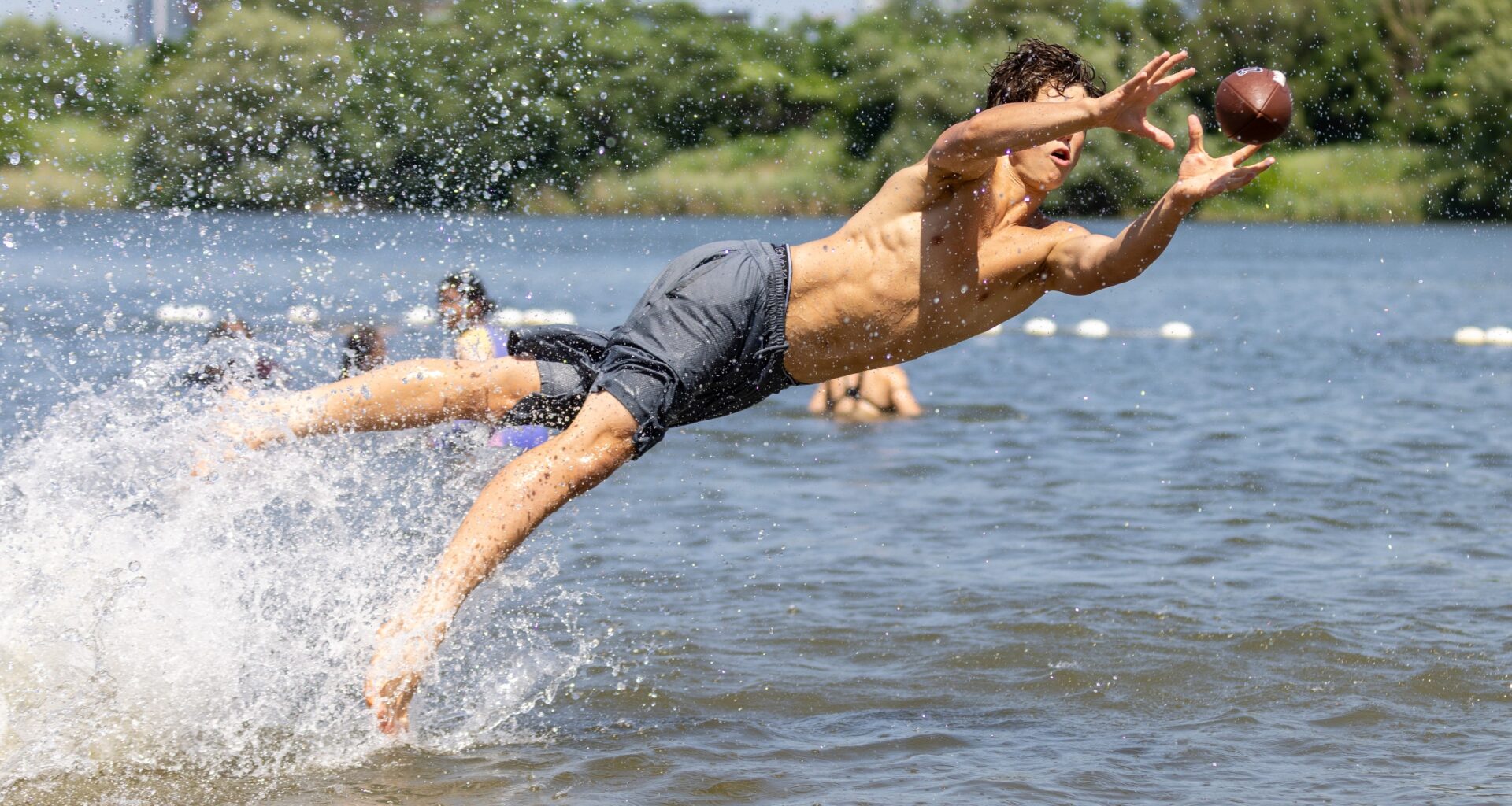 A man jumps nearly horizontally out of the water to catch a football