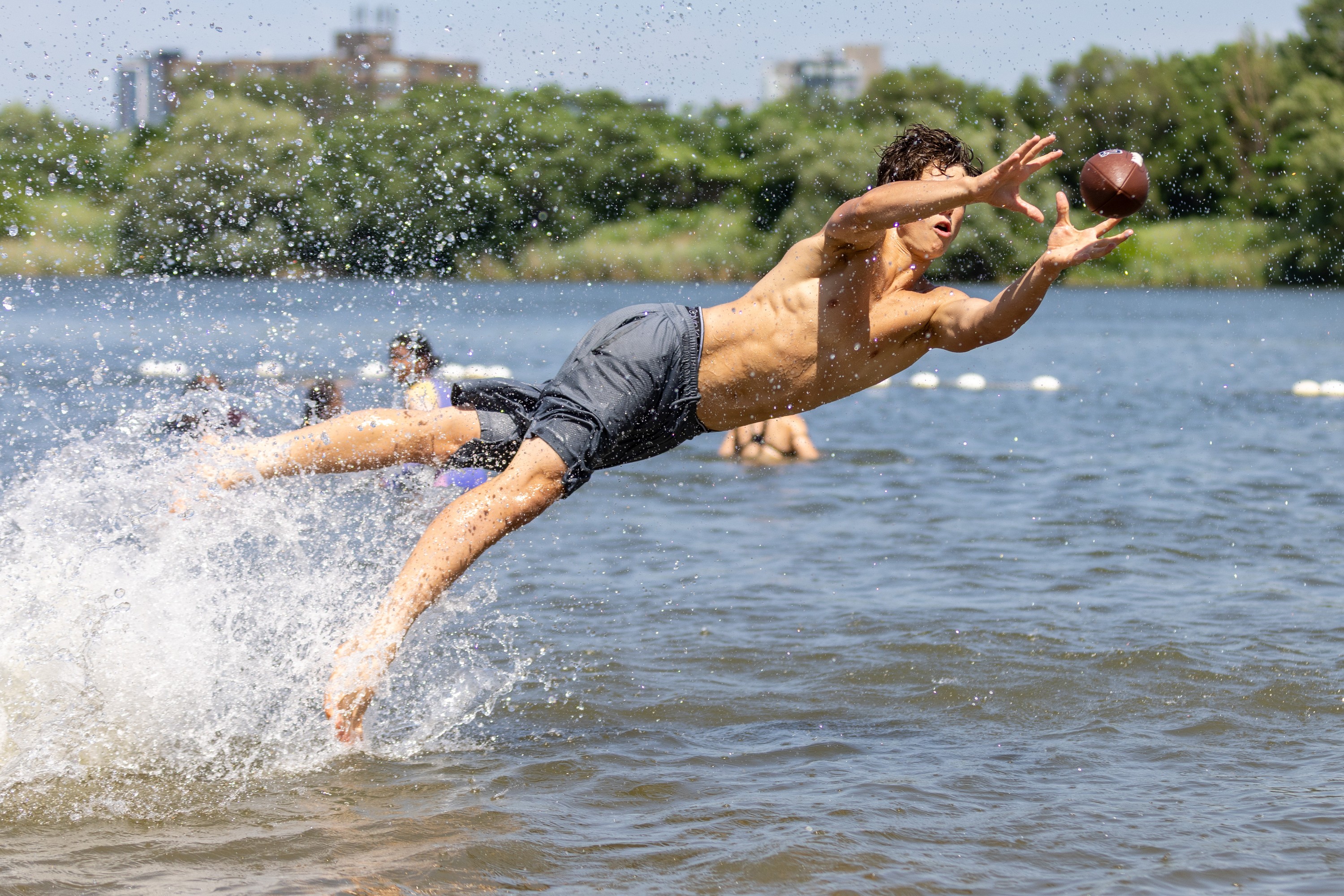 A man jumps nearly horizontally out of the water to catch a football