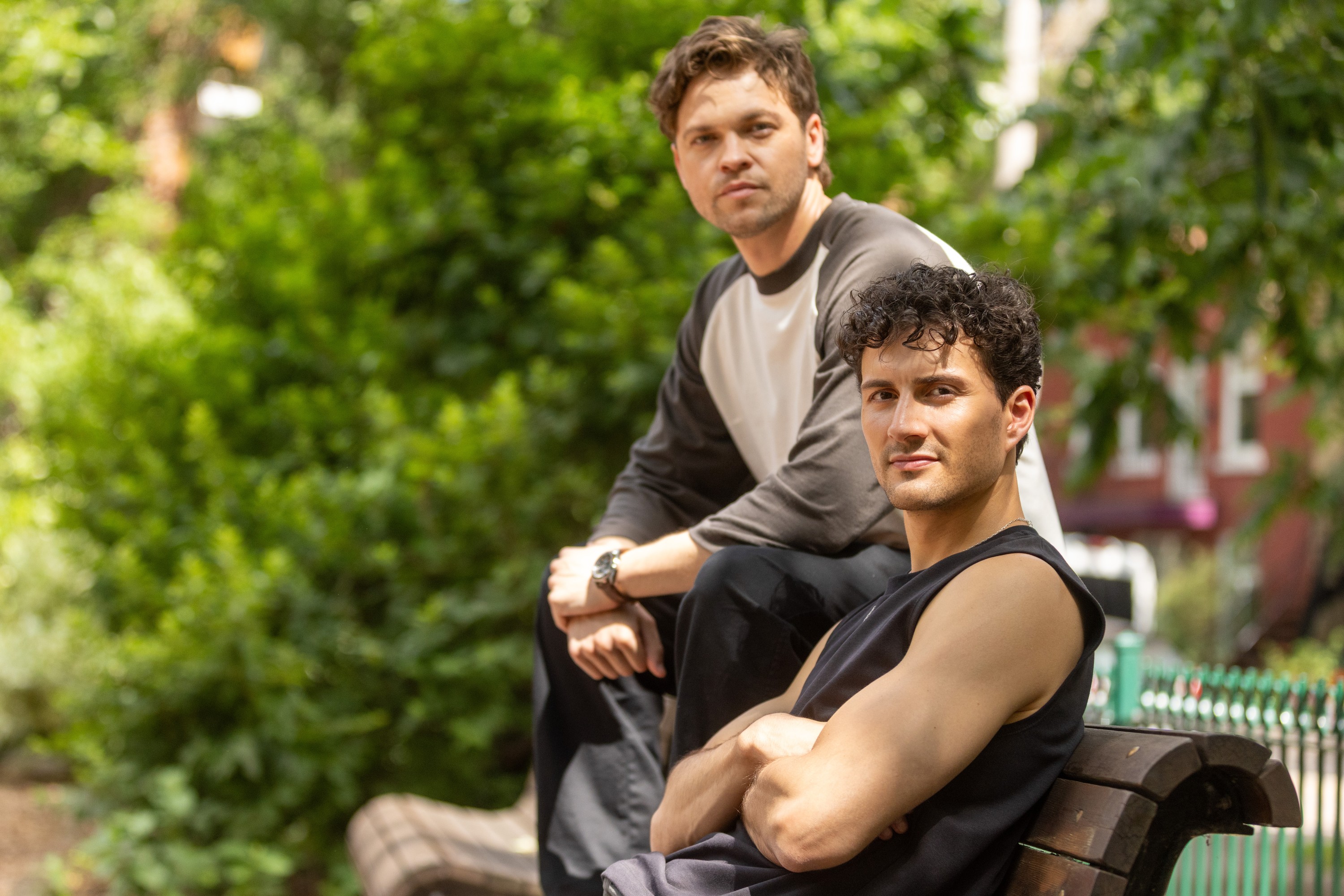 Two male actors pose with trees in the background. 