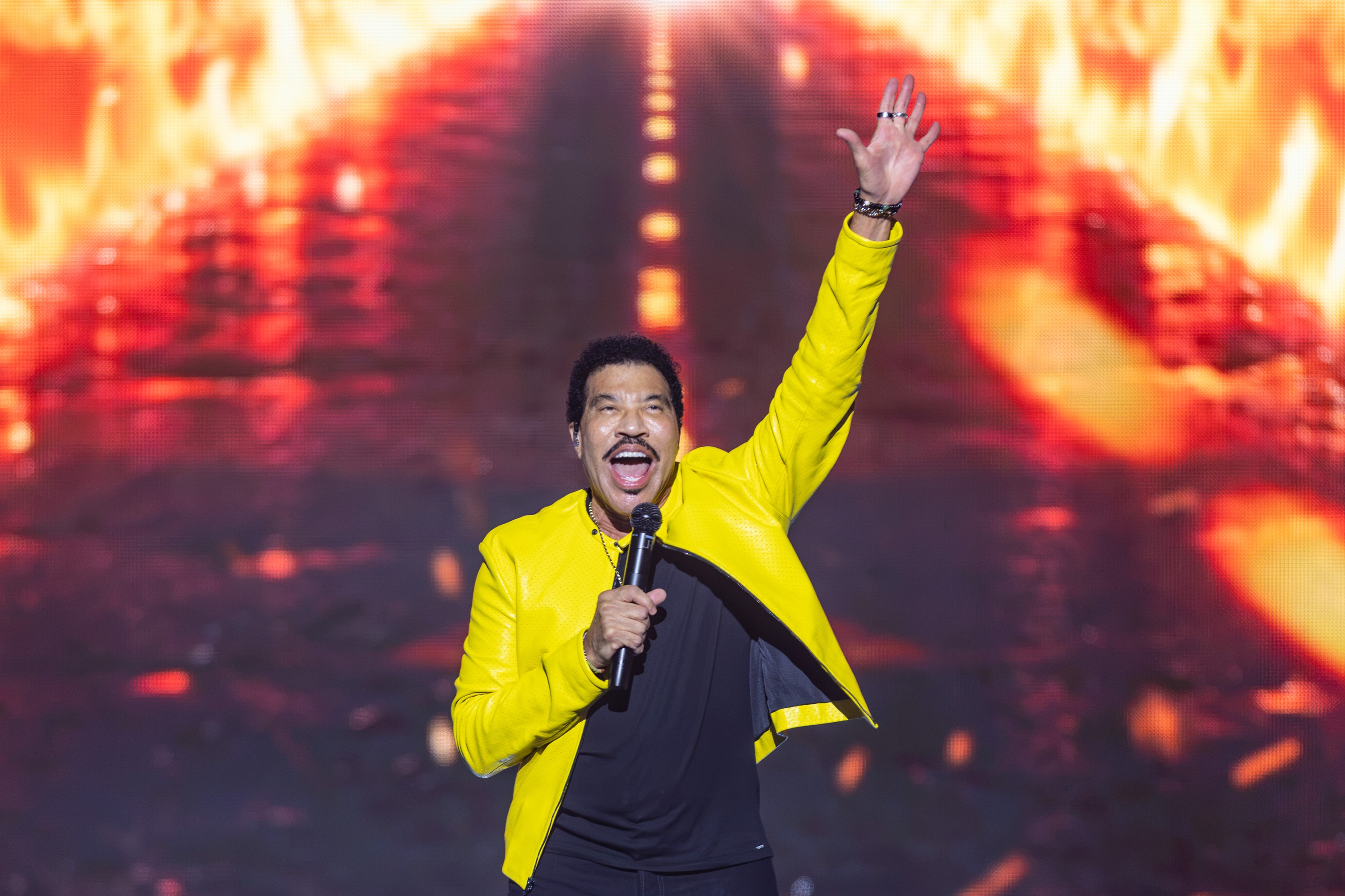 Lionel Richie raises a hand as he sings on stage.