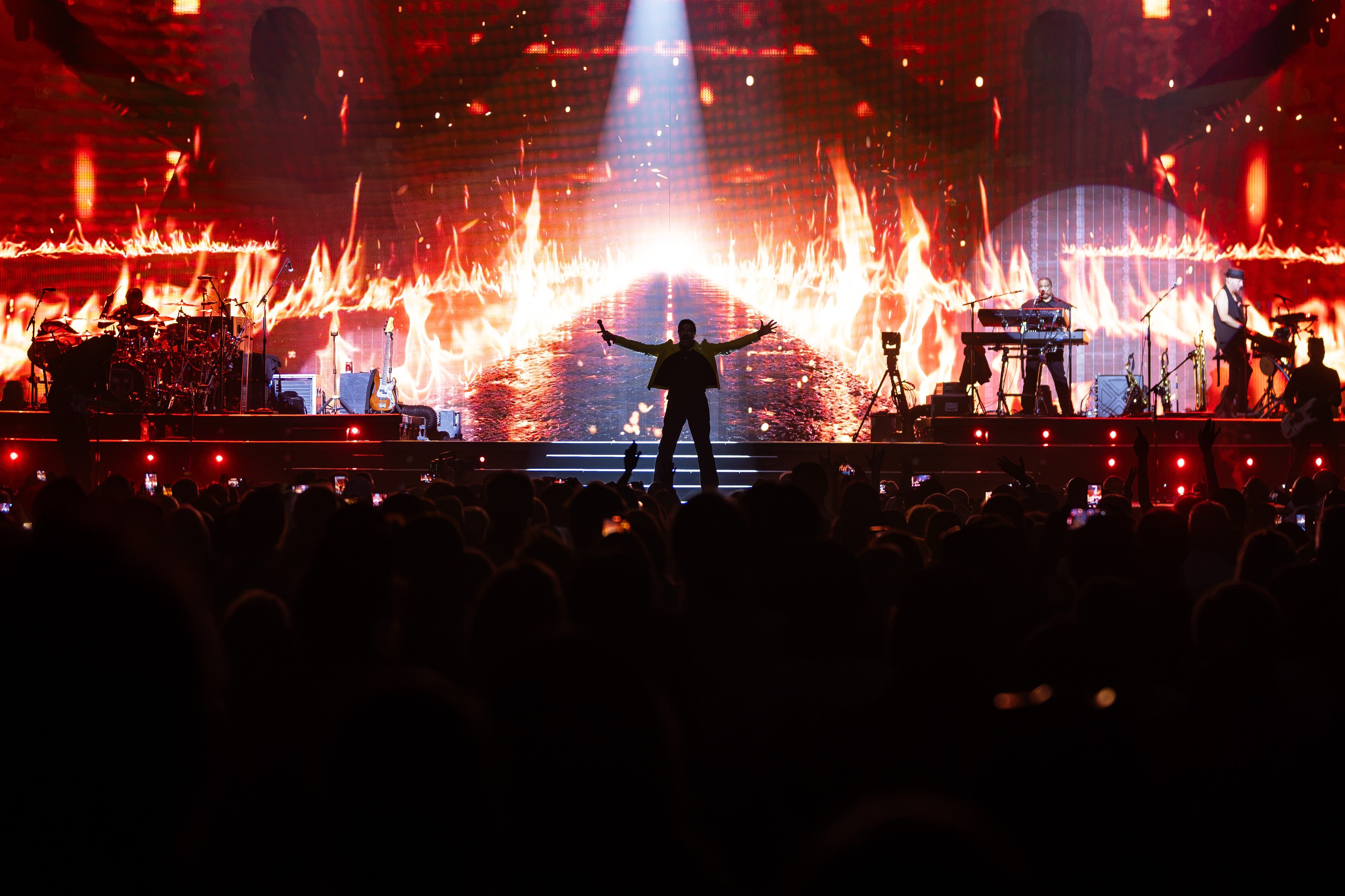 The outline of Lionel Richie is seen against a screen projection of flames as he performs on stage.