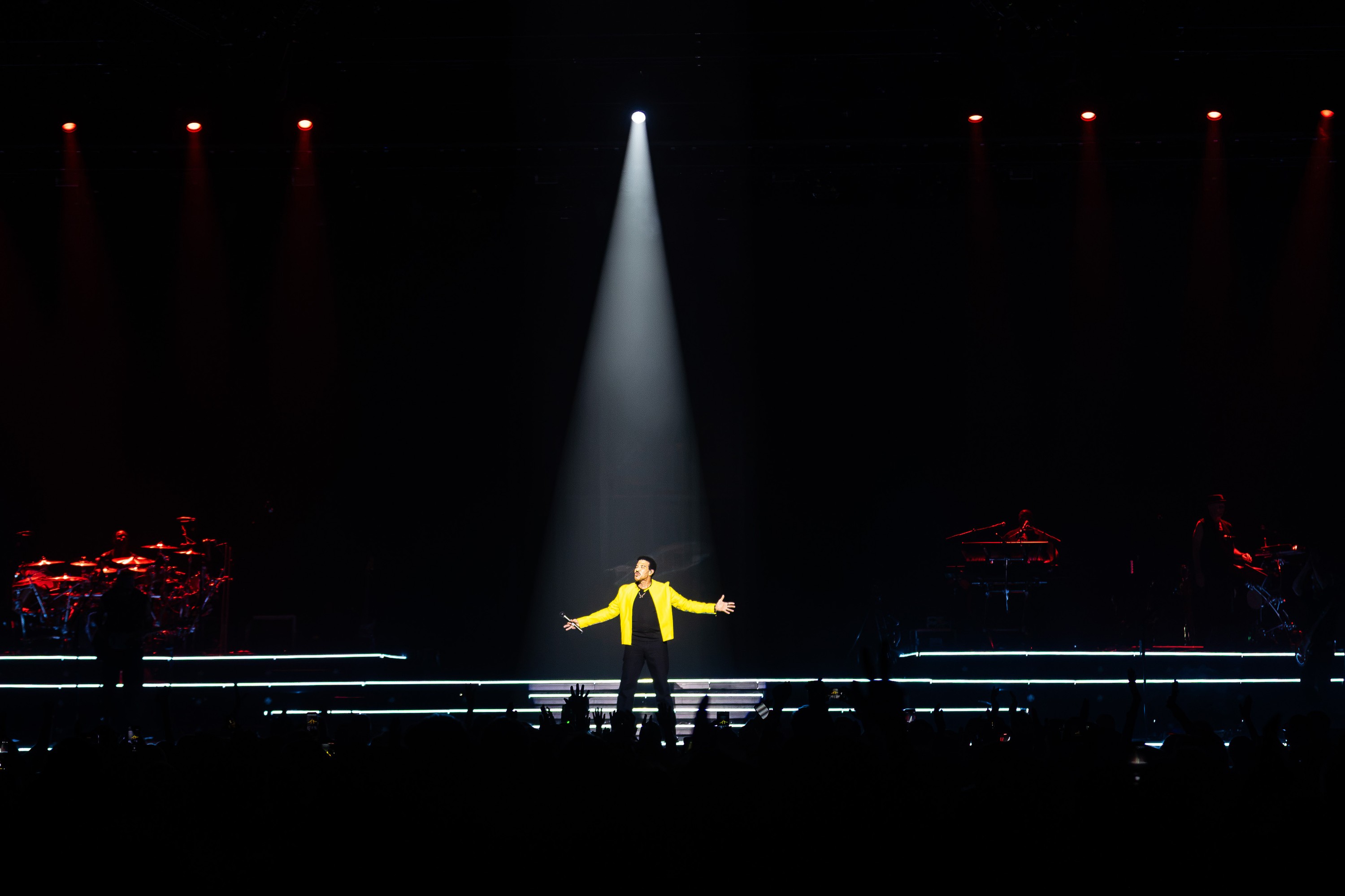 Lionel Richie, under a spotlight in front of a stadium crowd.