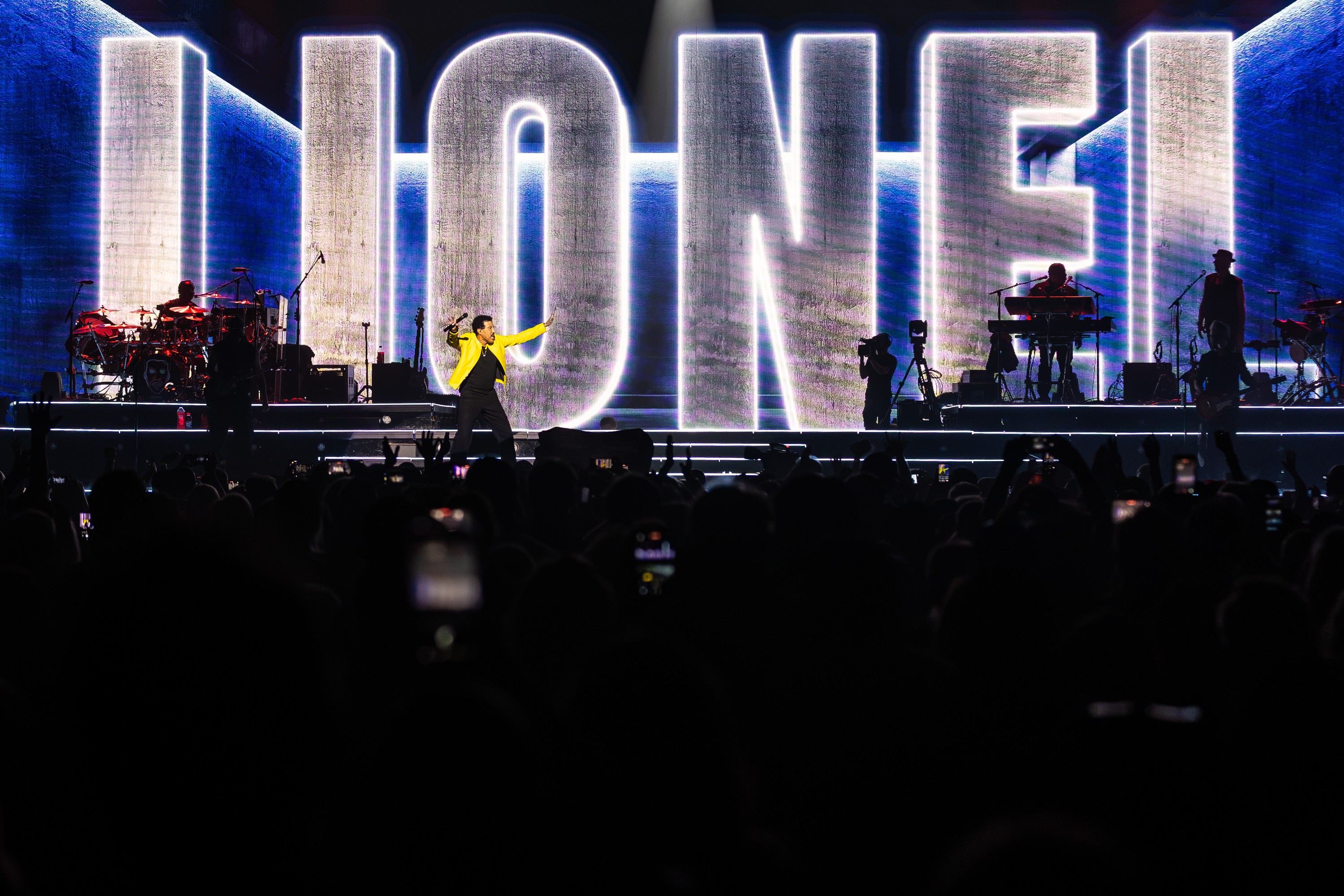 Lionel Richie on stage in front of a giant projection of his name.