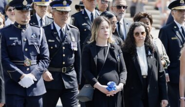 A pregnant woman wearing black and holding a blue rose stands with a woman and several police officers in dress uniforms.