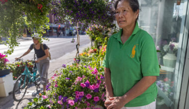 A woman stands outside a flower shop as a person on a bicycle cycles by.