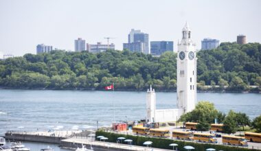 A clock tower is seen from altitude, looking out over docks and a river.