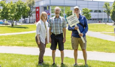 Three people stand on a grassy patch in front of IGA Stadium in Montreal's Jarry Park. One of them holds a sign saying Sauvons le parc Jarry