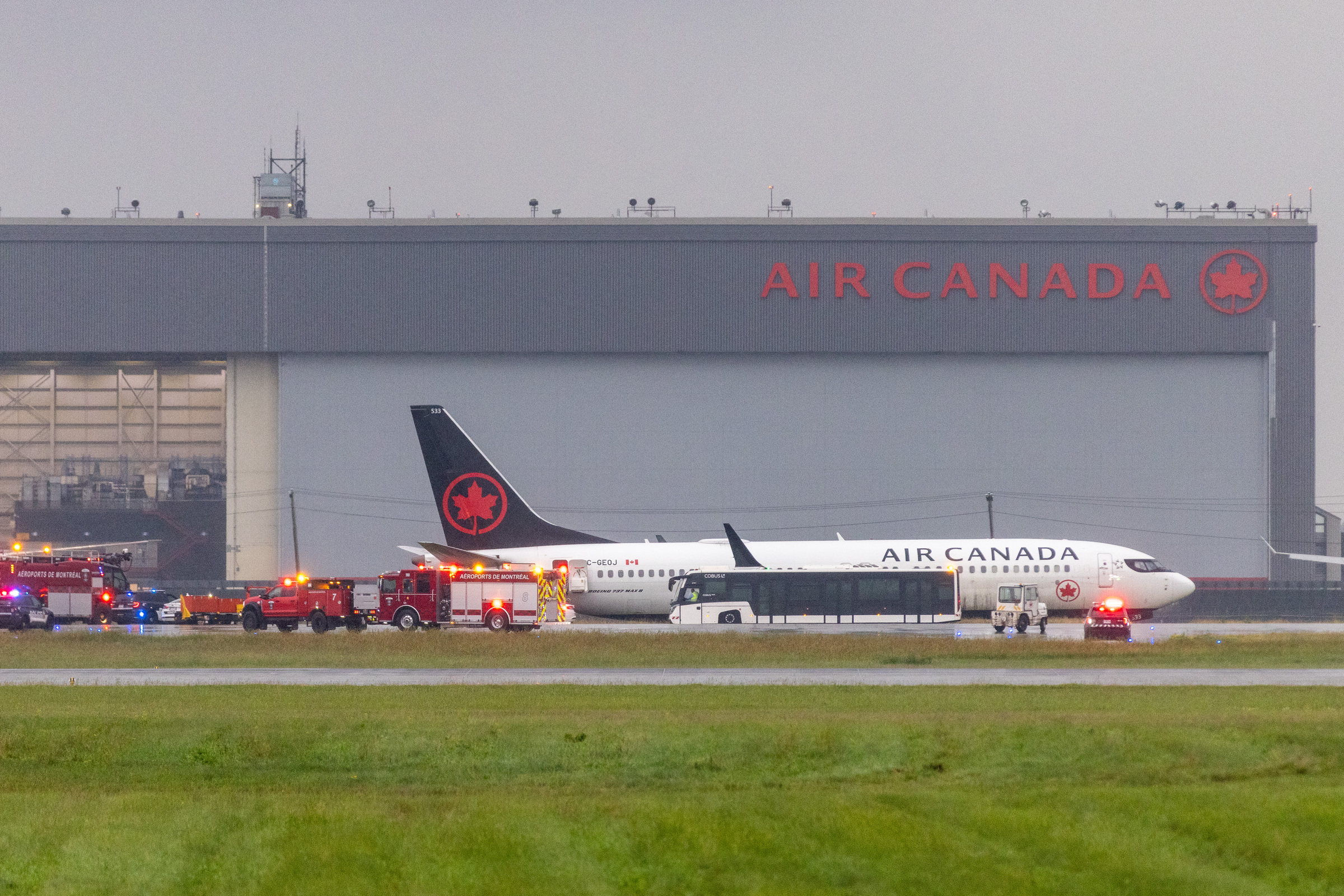 An Air Canada plane is visible with vehicles around it and an Air Canada hangar in the background.