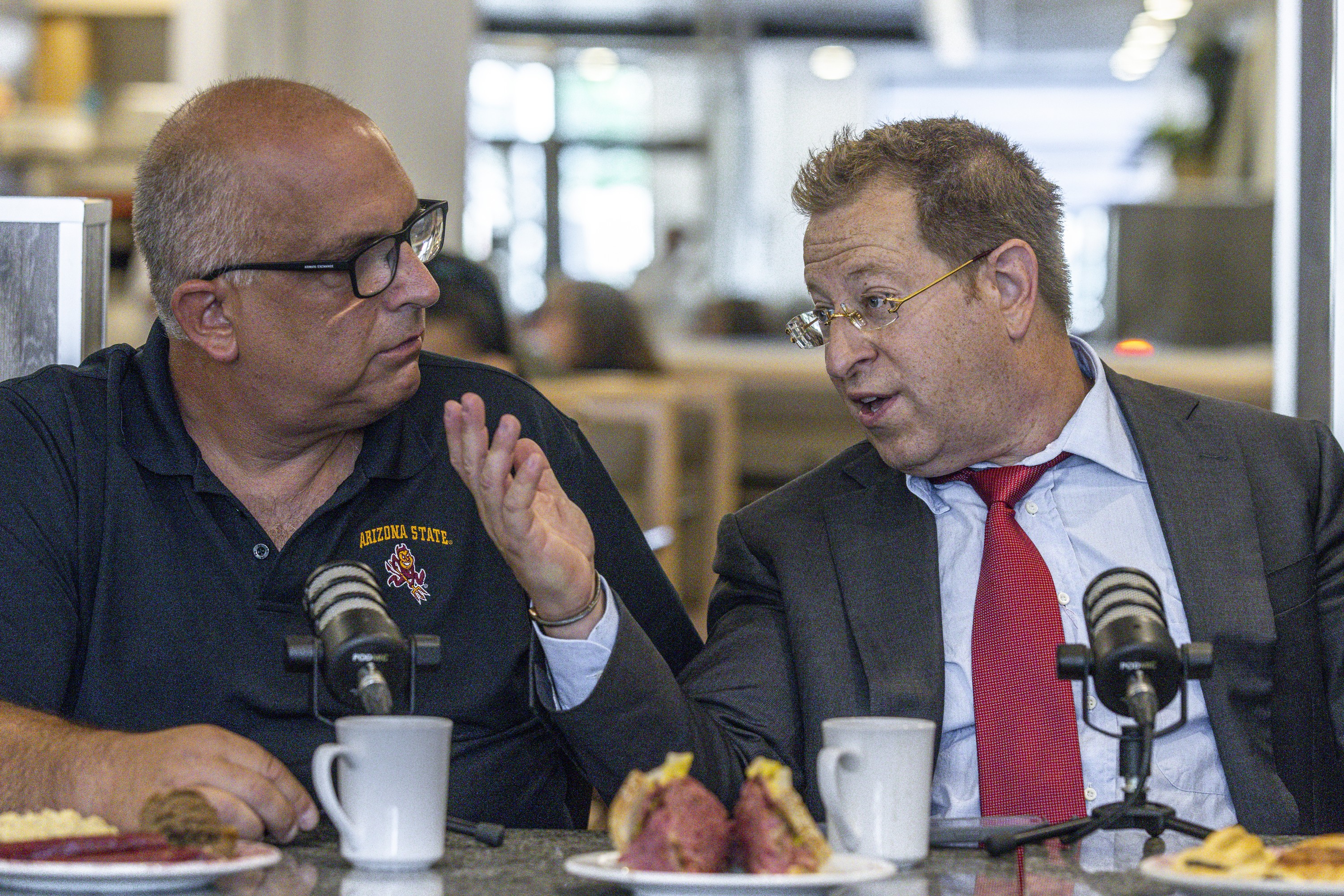 Two men sitting beside each other at restaurant table, talking.