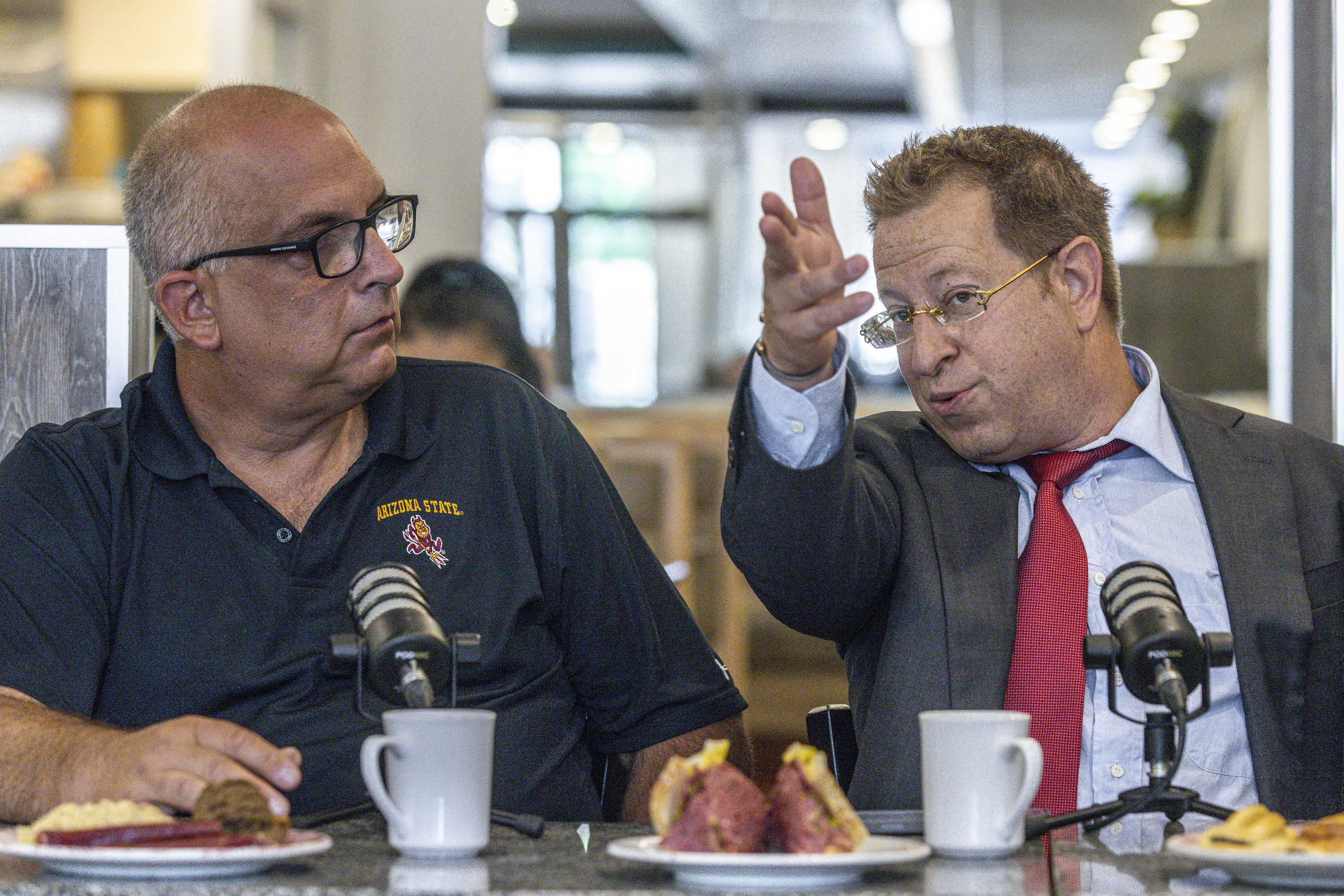 Two men sitting beside each other at restaurant table, talking.