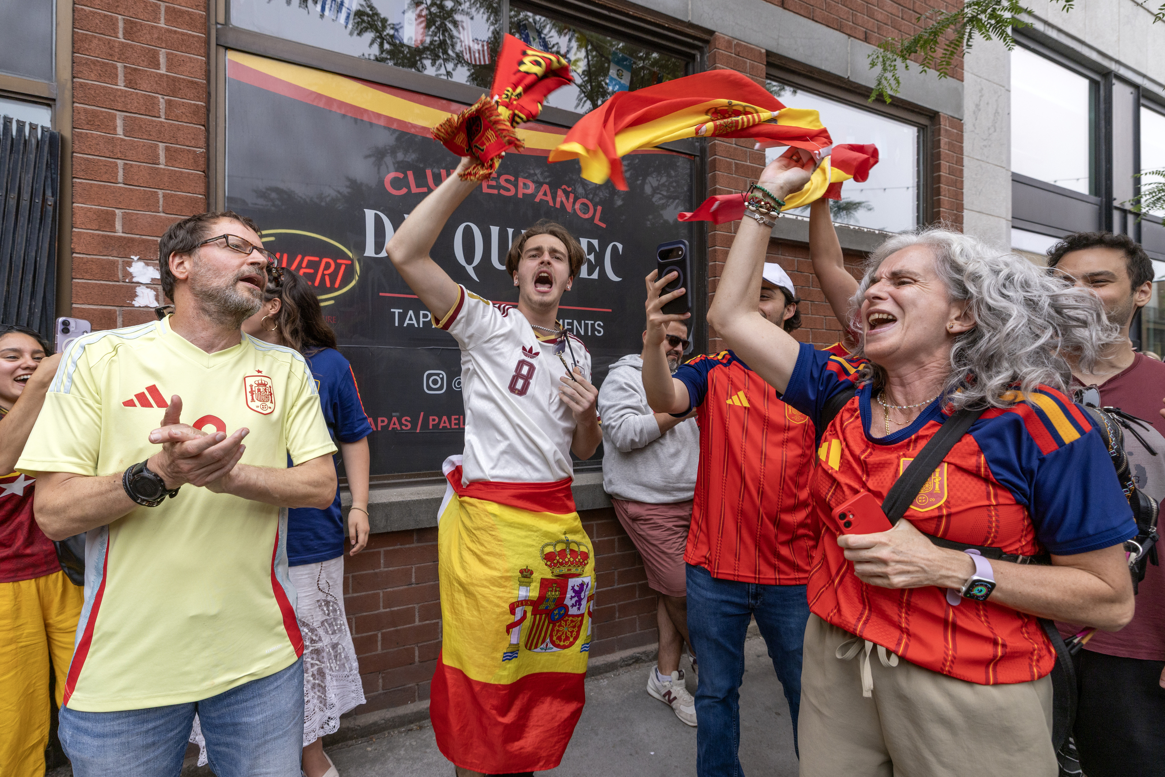 People celebrate while waving red and yellow flags outside.