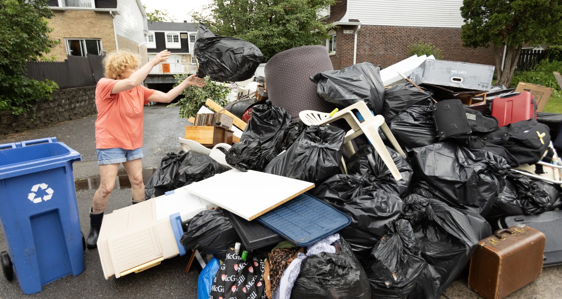 Risa Weigersberg throws a bag of garbage onto the growing pile of flood-damaged items outside her Dauphin St. home in Dollard-des-Ormeaux on June 21, 2026.