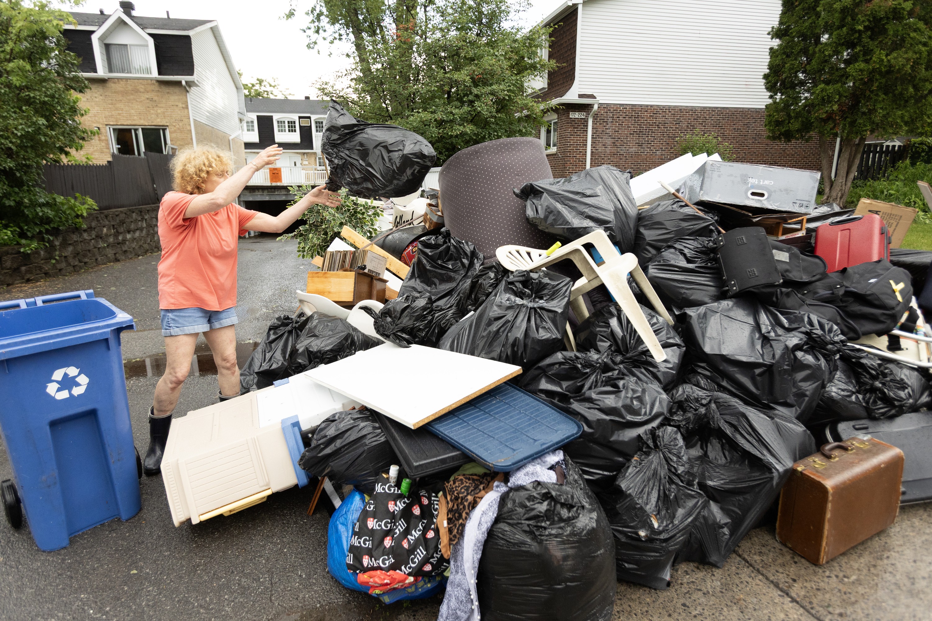 Risa Weigersberg throws a bag of garbage onto the growing pile of flood-damaged items outside her Dauphin St. home in Dollard-des-Ormeaux on June 21, 2026. 