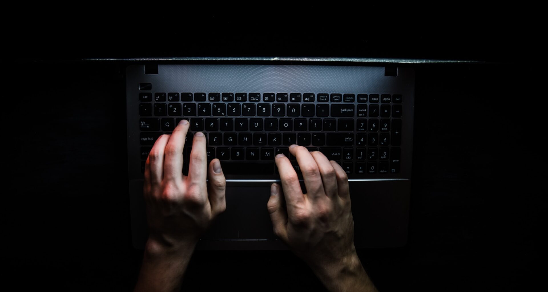 Hands on a laptop keyboard in the dark.