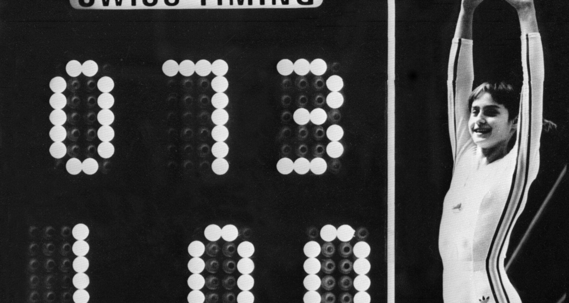 Romanian gymnast Nadia Comaneci celebrates on July 19, 1976 as the Montreal Forum scoreboard shows the perfect score of 10 – actually shown as 1.00, as the scoreboard wasn't built to show 10.00 – following her 1976 Montreal Olympic Games routine on the uneven bars.