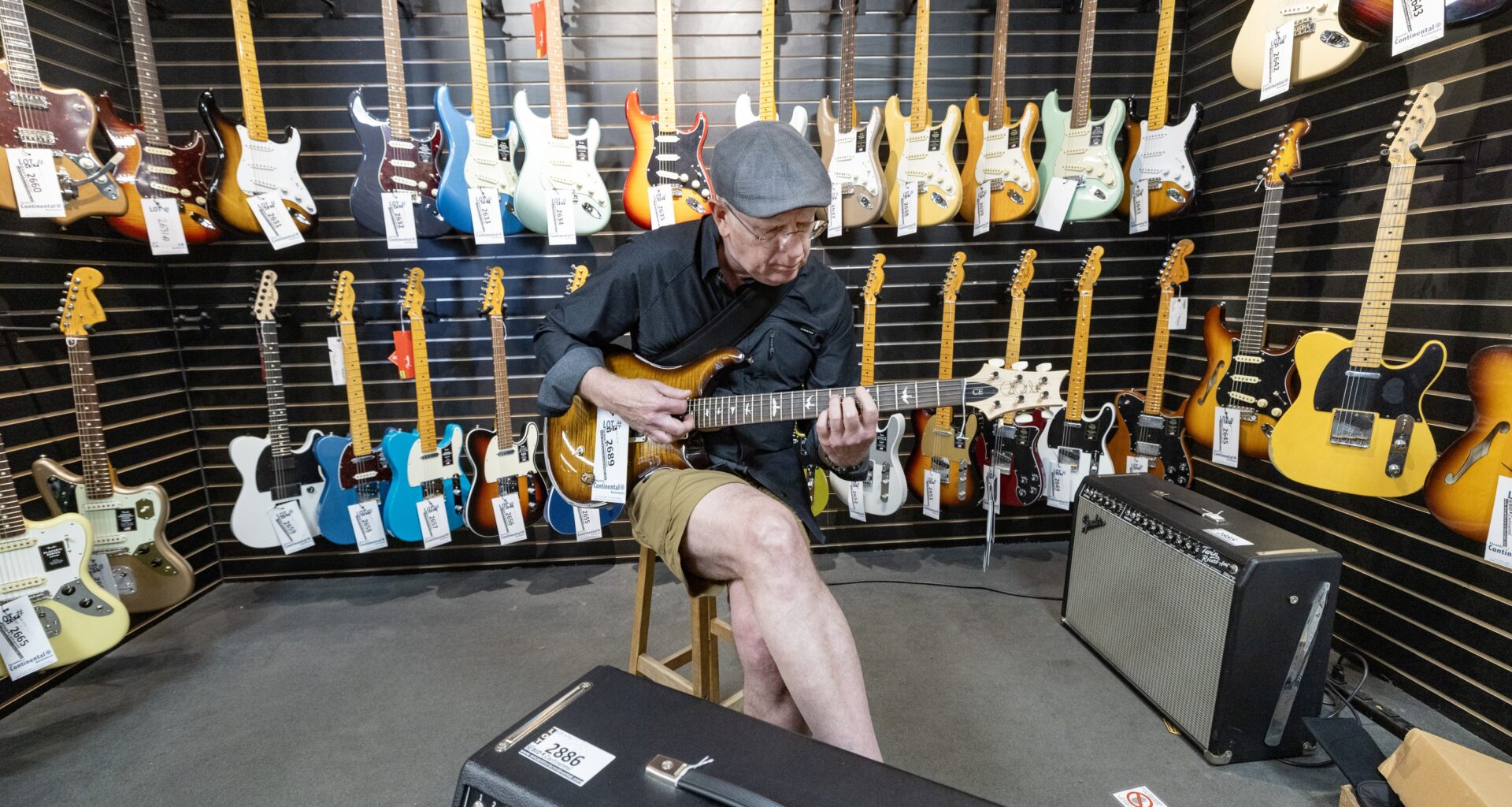A man tries an electric guitar as he sits in a music store in front of racks of other guitars