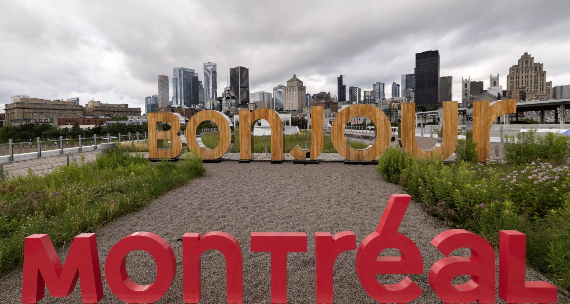 Large cutout signs read BONJOUR MONTREAL, with the city skyline in the background under cloudy skies.
