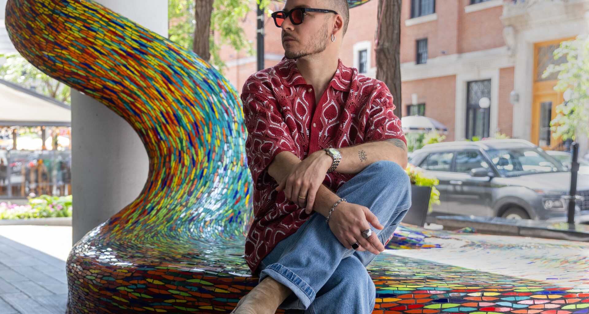 A man sits on the edge of an artwork on a sidewalk.