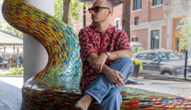 A man sits on the edge of an artwork on a sidewalk.